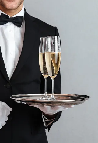 Serveur en smoking portant deux fl&ucirc;tes de champagne sur un plateau.