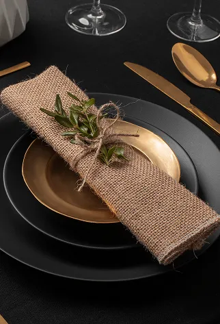Serviette en toile de jute sur assiette noire et dor&eacute;e, couverts dor&eacute;s.